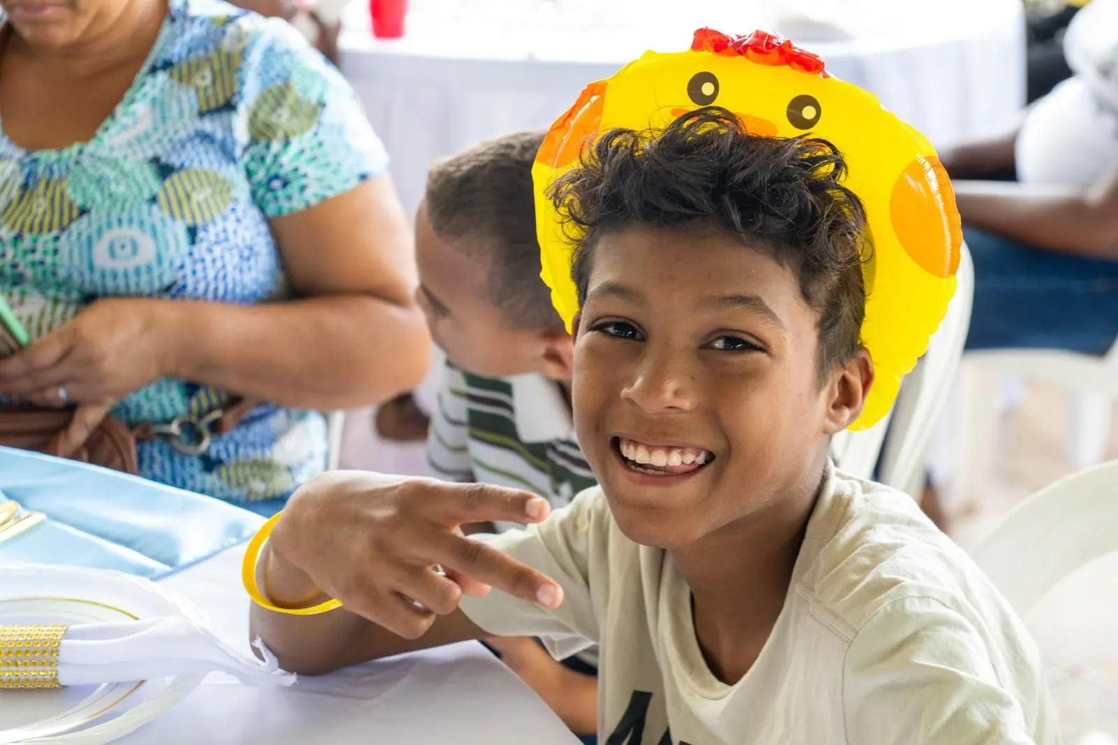 A boy in a duck balloon hat flashing a peace sign